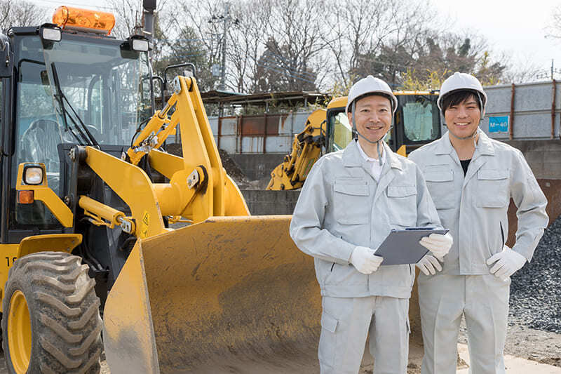 重機の前に立つ作業着の男性2人